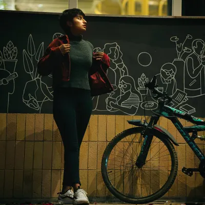 A stylish night portrait of a woman standing next to a bicycle against a wall with line art. The urban setting and dramatic lighting give this shot a cool, cinematic vibe.