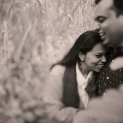A soft, grainy black and white photo that feels incredibly intimate and timeless. The focus is entirely on the couple's happy embrace, surrounded by tall grass.