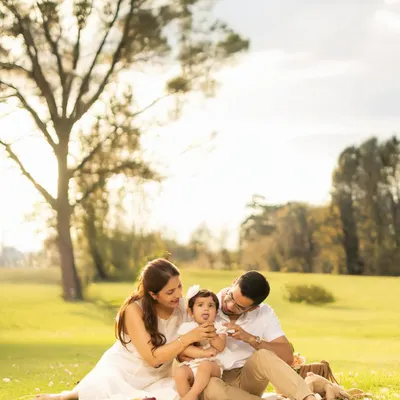 A sweet family picnic moment captured in warm, golden sunlight. This candid shot shows the parents lovingly interacting with their baby, creating a memory filled with tenderness and natural beauty.