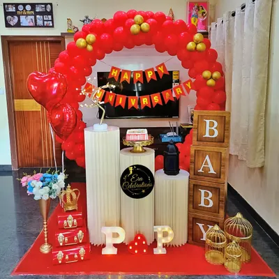 A classic red and gold anniversary setup for a celebration at home. It features a red balloon arch, white plinths for the cake, and marquee letters.