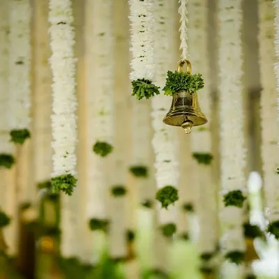 A close-up of hanging floral decor, featuring strings of white chrysanthemums and a single brass temple bell. This simple detail adds both visual beauty and a touch of serene sound to the ambiance.