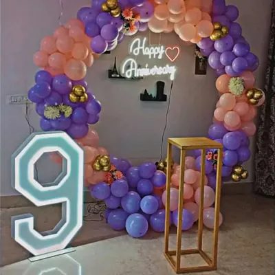 For this 9th anniversary, I created a beautiful circular balloon arch using purple, peach, and gold balloons. The setup includes a 'Happy Anniversary' neon sign and a large light-up number '9' to mark the special occasion.