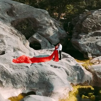 An aerial view showcasing the sheer drama of our red infinity trail gown. The vibrant color pops against the natural rock formations, creating a breathtaking shot for any couple.