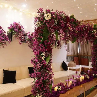 This stunning floral arch, created in a deep purple and magenta palette, became the centerpiece of the living room for a special celebration. It's paired with a matching table runner and fairy lights.