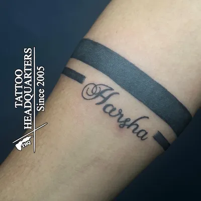 A classic armband tattoo personalized with the name "Harsha" in a beautiful cursive script, integrated into the solid band design.