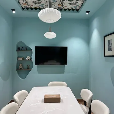A view of our newly revamped studio's meeting room. The space features calming blue walls, a ceiling with floral wallpaper, and a large marble-finish table for client consultations.