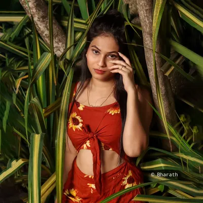 An outdoor portrait using dense, leafy foliage as a natural backdrop. The vibrant greens make the subject's red outfit pop.