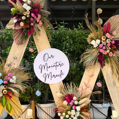 A stunning boho-chic baby shower backdrop. We used triangular wooden frames adorned with vibrant dried florals, pampas grass, and a sign celebrating "Our Miniature Miracle."
