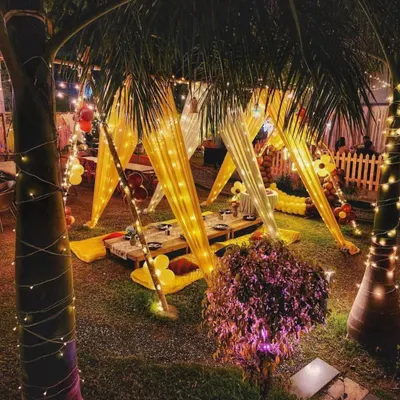 A beautiful nighttime view of a garden party setup, with canopy tents illuminated by fairy lights, creating a warm and inviting atmosphere.