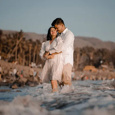 Komal and Ajit share a tender embrace while standing in the gentle waves of the sea. The warm golden hour light makes this beach pre-wedding photo incredibly romantic.
