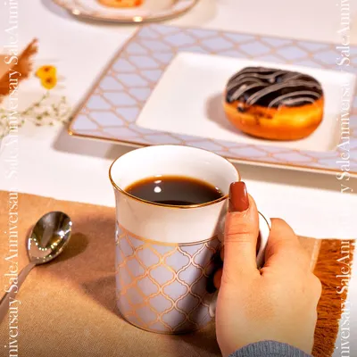 A quiet moment of indulgence with my Ichkan tableware. This image captures a hand reaching for a coffee mug, with a donut and cupcake served on plates featuring a delicate blue and gold lattice pattern.