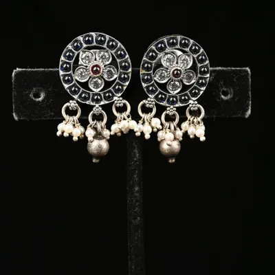 These authentic 92.5 silver earrings feature a circular design with intricate filigree work and a central stone. The dangling pearl and silver beads add a touch of playful elegance.