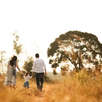 A beautiful shot of a family of three walking away from the camera into a sun-drenched field, holding hands.