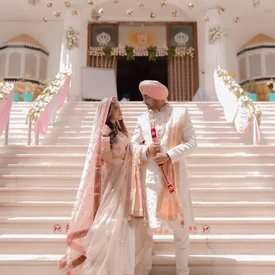 A majestic portrait of a Sikh couple on the steps of the Gurudwara. Their pastel pink outfits are the picture of elegance against the grand white architecture.
