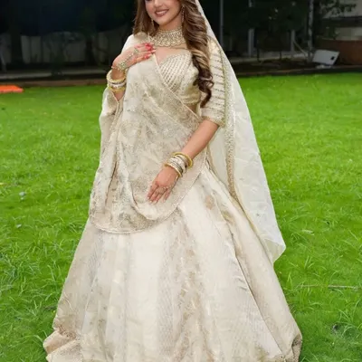 A full-length view of a bride in a magnificent ivory and gold lehenga. The look is completed with a matching choker, bangles, and a delicate matha patti for a truly royal feel.
