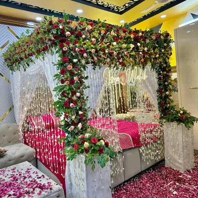 A beautiful welcome bride setup featuring a canopy rich with red and pink florals, complemented by hanging crystal strings and a personalized neon sign for the couple.