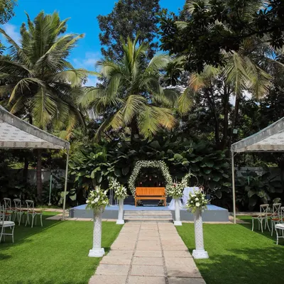 A beautiful daytime wedding setup at Farmhouse Collective, with the aisle leading to a floral-adorned bench on the stage. The surrounding palm trees and greenery create a perfect tropical oasis in Bangalore.