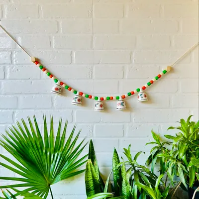 Our 'Khanak' beaded bell bunting in a festive red and green combination. This 30-inch wide bunting features five delicate mini ceramic bells and colorful wooden beads, perfect for adding charm to your entrance or temple space.