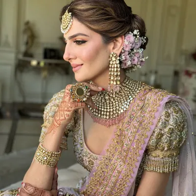 A classic bridal look featuring a soft, textured low bun. I adorned this updo with a semi-circle of fresh pink and white flowers to match the bride's pastel lehenga, creating a look of pure elegance.