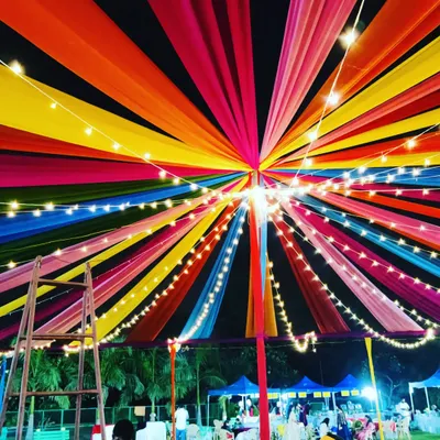 A close-up view from underneath the massive Dandiya night canopy. The radiating strips of colorful fabric are interwoven with bright string lights, showing the detailed craftsmanship that goes into our large-scale festive decorations.