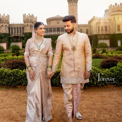 A fairytale moment at the Bangalore Palace. The groom's cream sherwani with a subtly contrasting pastel pink dhoti and stole was designed to match the delicate, intricate embroidery on the bride's breathtaking saree.