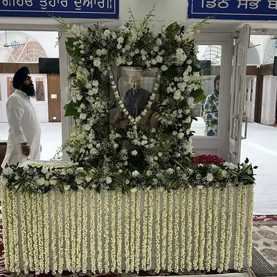 A respectful floral setup for a prayer meeting. The portrait is framed with fresh white flowers, and the table is adorned with jasmine strings, creating a peaceful ambiance for remembrance.