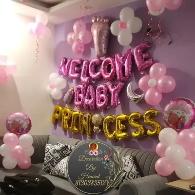 A "Welcome Baby Princess" decoration for a home celebration. The wall is decorated with pink and white balloons, flower-shaped balloon clusters, and large foil letters spelling out the welcome message.