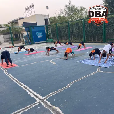 Our students practicing the downward dog pose during an outdoor yoga session. This helps improve flexibility in the hamstrings and shoulders, crucial for basketball players.