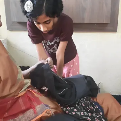 An older family member passes down the skill of sewing to a young girl. We believe in intergenerational learning and the value of preserving traditional repair skills like mending clothes.