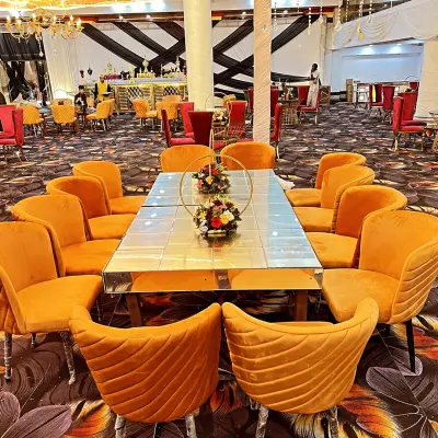 This is a long dining table setup for guests, featuring a mirrored tabletop that reflects the decor. The comfortable orange velvet chairs add a pop of color to the event space.