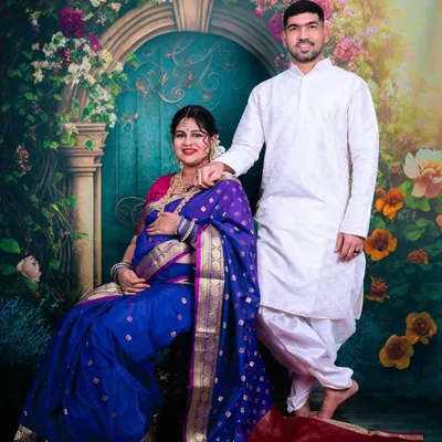 A beautiful couple portrait from a traditional maternity shoot in our studio. The mother-to-be is seated gracefully in a royal blue saree, complemented by a floral archway backdrop.