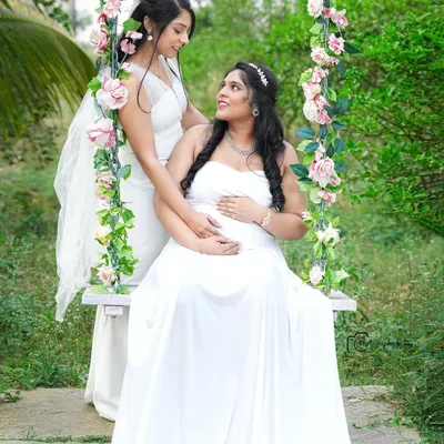 A beautiful moment between sisters or friends celebrating the upcoming arrival. Both are dressed in elegant white gowns, sharing a look of love and support.