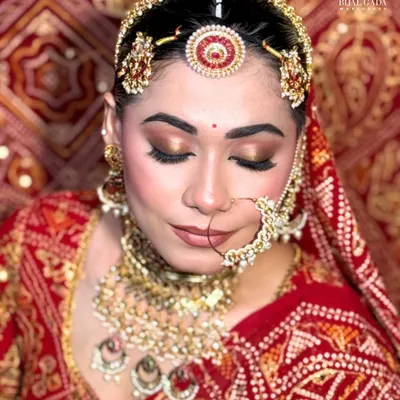 A close-up of the Marwadi bridal makeup, focusing on the golden-bronze eyeshadow that complements the red 'borla' and intricate nath. The look is all about rich colors and flawless skin.