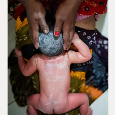An overhead view of a traditional newborn oil massage, a moment of pure, tender care. We document these intimate rituals with respect and artistry, focusing on the loving touch.