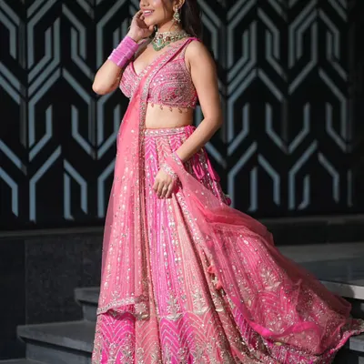 A vision in pink. This look pairs a beautifully embroidered pink lehenga with a statement choker featuring a large green stone and sparkling zircons, perfect for a sangeet or reception.
