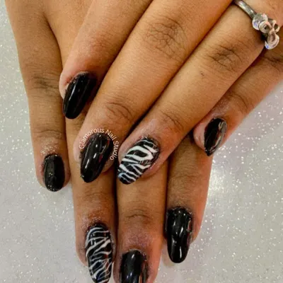 A walk on the wild side. This edgy design features a glossy black polish with accent nails showcasing a classic black and white zebra print.