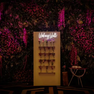 A "Wishing Wall" set against a dramatic backdrop of purple-lit foliage. This interactive station allows guests to leave heartfelt messages for the hosts, making it a meaningful addition to any celebration.