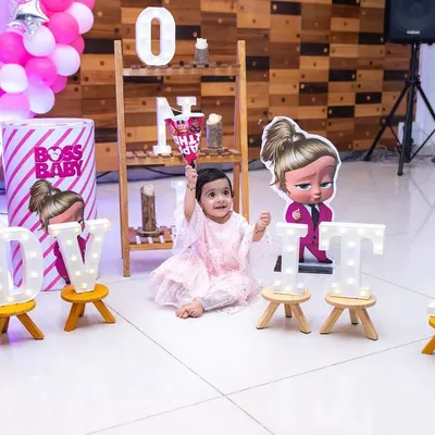 A one-year-old girl sits amidst her 'Boss Baby' themed birthday decorations, complete with marquee lights spelling her name. We excel at capturing solo portraits of the birthday star within their party setup.