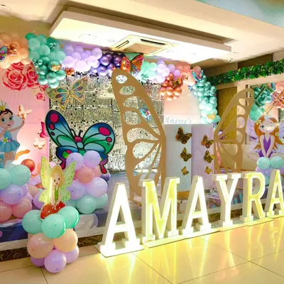 A wide view of our elaborate Butterfly Garden birthday setup. It features a stage with illuminated letters, large wooden butterfly wings, fairy cutouts, and extensive balloon sculptures in pastel shades.
