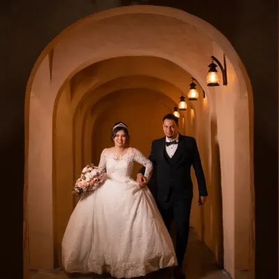 A fairytale entrance. The couple walks hand-in-hand through a warmly lit archway, beginning their life together.
