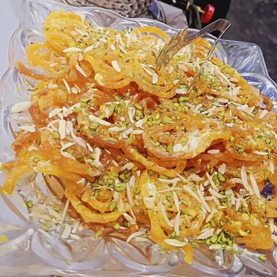 A close-up of my perfectly crisp and syrupy jalebi, garnished with chopped pistachios and almonds. It’s a classic dessert that I make fresh for my events.