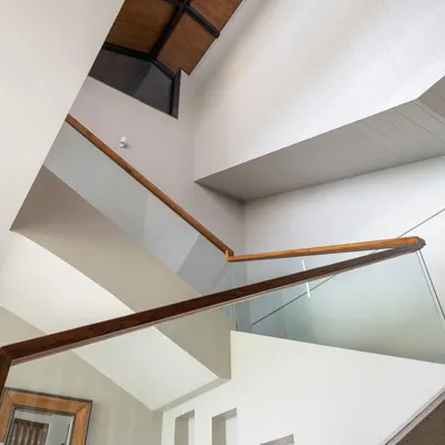 The double-height staircase in Grove House creates a sense of spaciousness and light. The clean lines of the glass and wood railing are a modern counterpoint to the home's tropical setting.