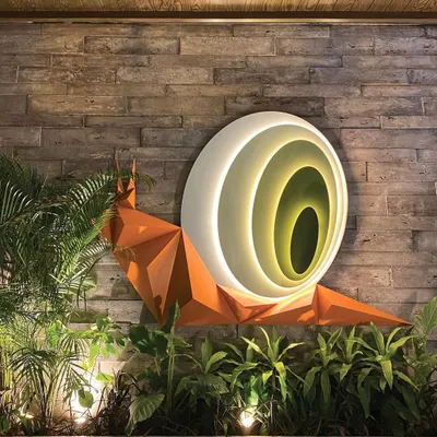 This biophilic snail art installation, titled 'Harmony in Motion,' is nestled within a landscaped court. The origami-like form and internal lighting create a captivating sense of wonder and tranquility, especially at night.