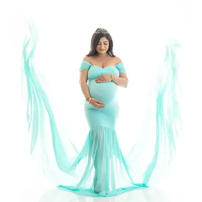 A full-length portrait of an expecting mother in a light blue gown, with flowing fabric creating a beautiful frame. The bright white background keeps the focus entirely on her.