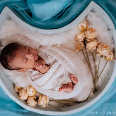 A peaceful newborn nestled in a moon-shaped prop. The soft white fur, gentle swaddle, and delicate dried yellow roses create a dreamy and serene setting for this baby portrait.