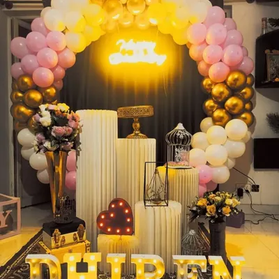 A beautiful birthday setup with a pink, white, and gold balloon arch. The arrangement of pedestals and props creates a balanced and elegant look.