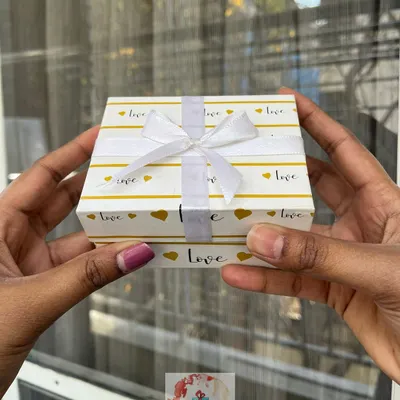 A small, elegant gift box with a "love" and gold heart pattern, tied with a delicate white ribbon. It's the perfect size for a small, intimate Valentine's Day present or a token of affection.