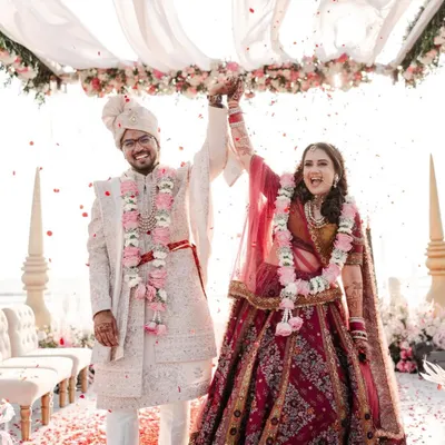 A perfect beach wedding moment. This happy couple celebrates under a canopy of flowing white fabric and pastel florals, with the beautiful Goa coastline in the background.