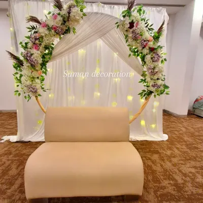 An elegant and romantic backdrop for a bridal shower or engagement. A circular gold frame is decorated with beautiful artificial flowers and greenery, set against a white curtain with fairy lights.