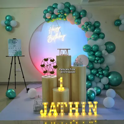 A beautiful first birthday setup for Jathin. This decoration features a teal and white balloon arch against a circular backdrop, with a light-up number '1' and name letters.